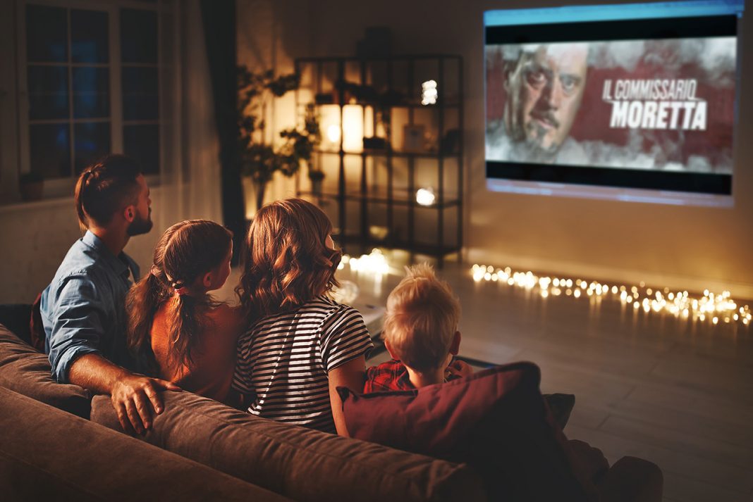 family mother father and children watching projector, TV, movies with popcorn in evening at home
